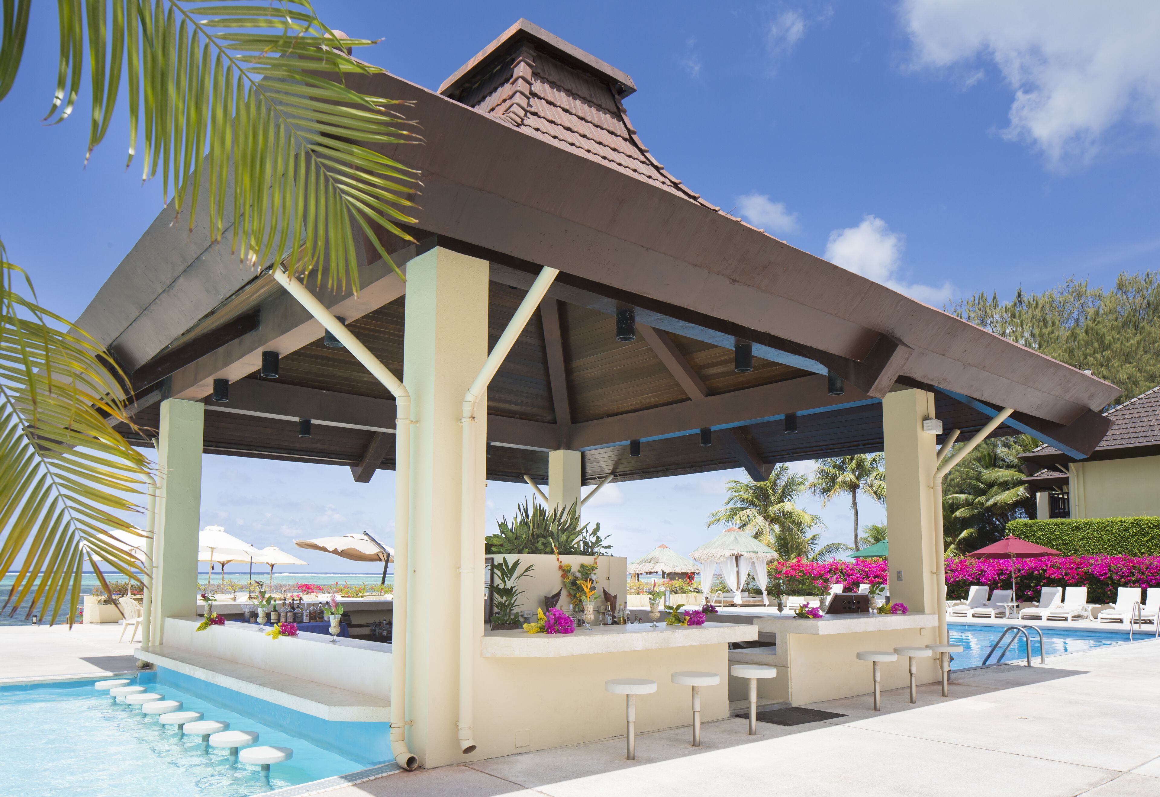 A covered pool area with a bar, lounge chairs, and a view of the ocean.