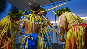 A group of people in traditional attire with long, green, leaf-like headdresses and wooden staffs. - Aqua Resort Club Saipan (Saipan)