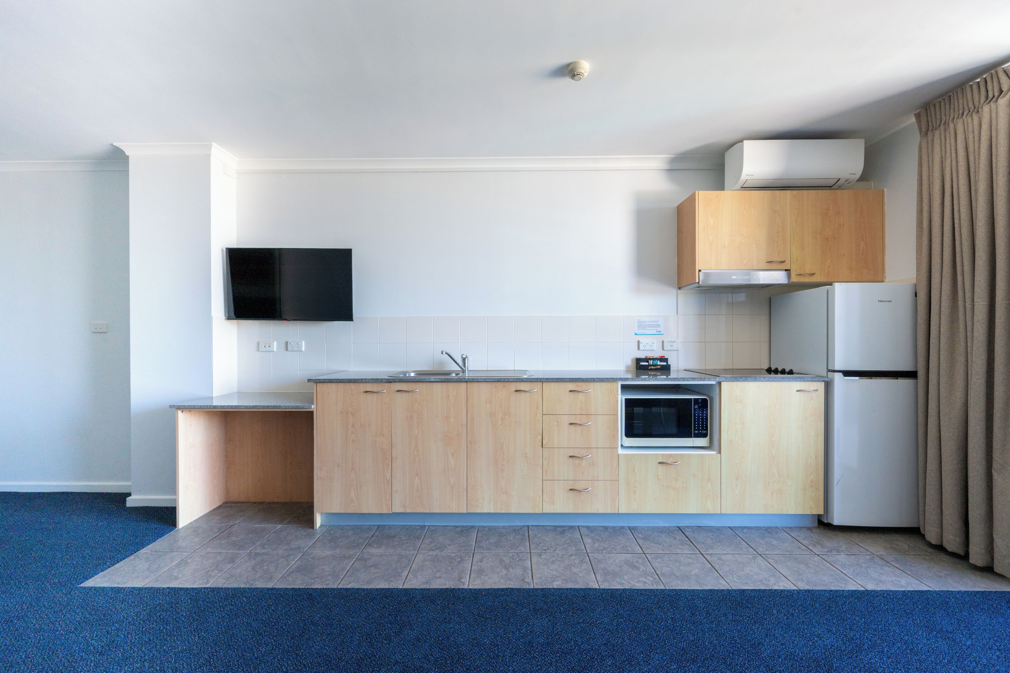 A modern kitchen with wooden cabinets, a built-in oven, a microwave, and a refrigerator.