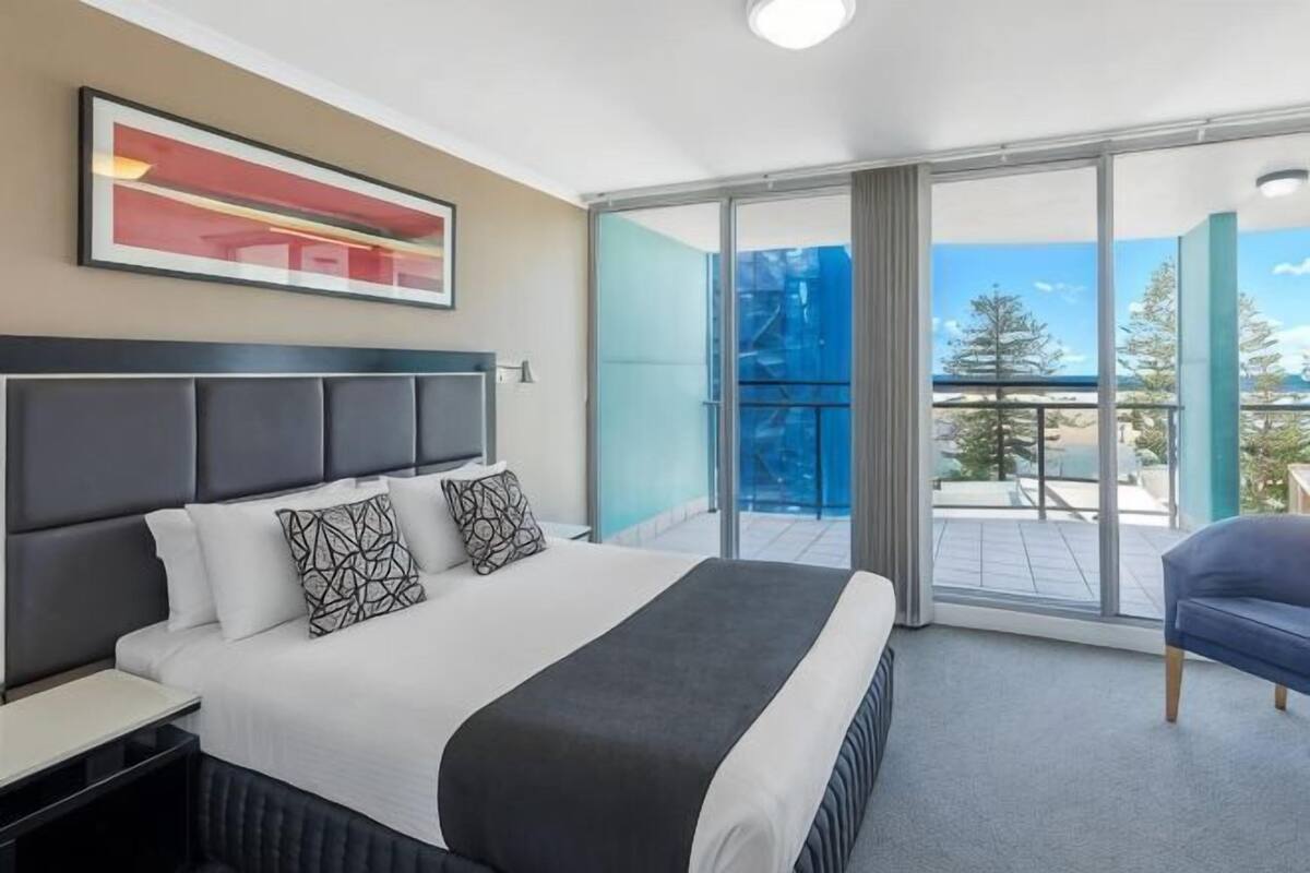 Een hotelkamer met een bed, nachtkastje, stoel, groot raam en balkon.
