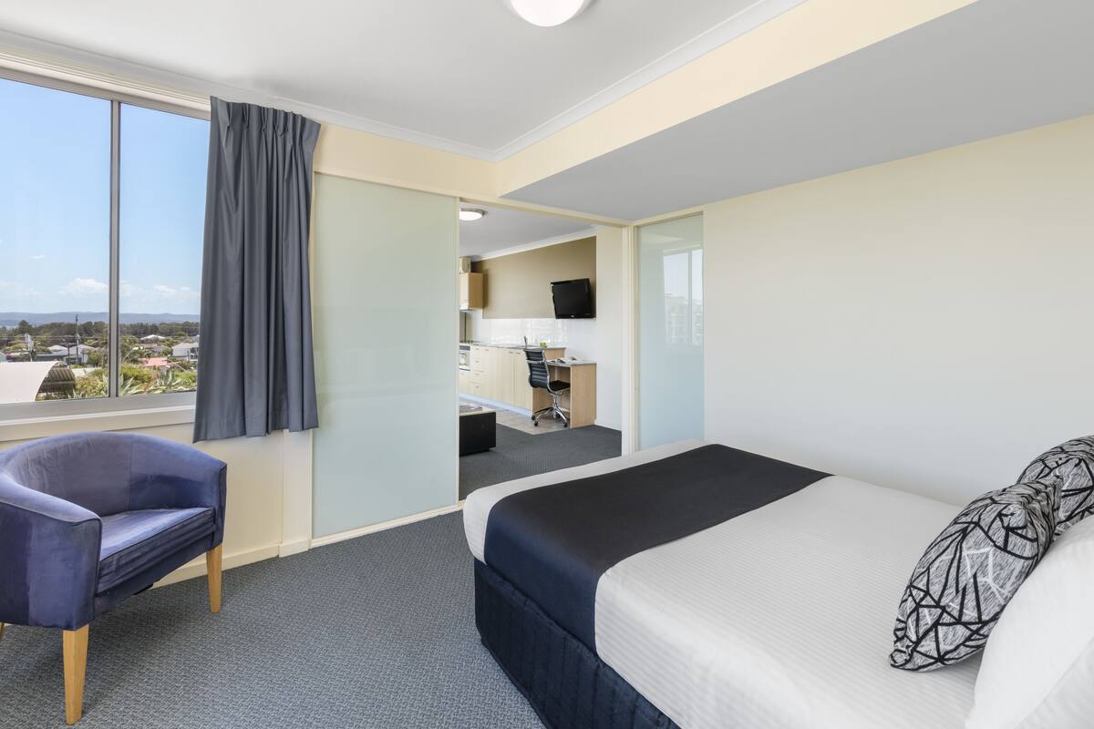 Een hotelkamer met een groot bed, een stoel, een bureau en uitzicht op de stad.