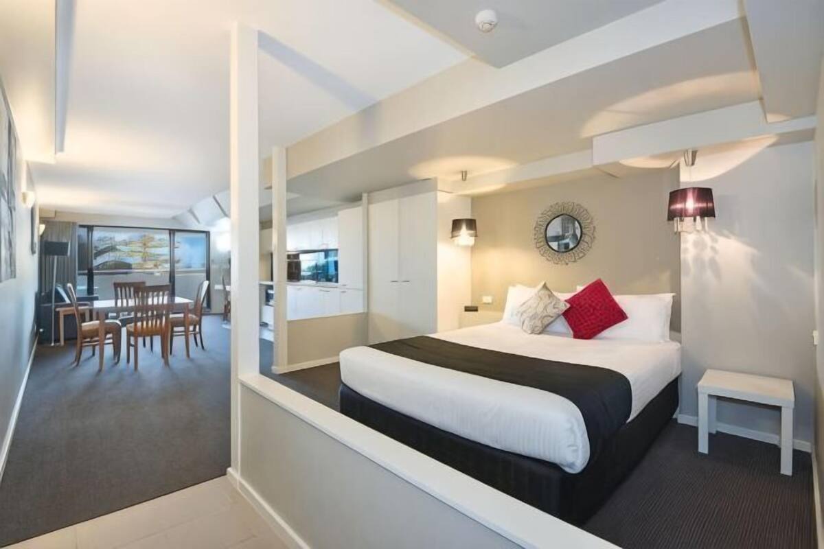 Een moderne hotelkamer met een groot bed, een klein nachtkastje, een zithoek met stoelen en uitzicht op de stad.