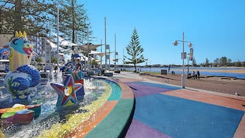 A colorful water fountain with a dragon and starfish design, surrounded by a playground area with various play structures.