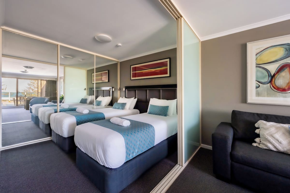 Een hotelkamer met drie bedden, een bank, een grote spiegel en kunstwerken aan de muur.
