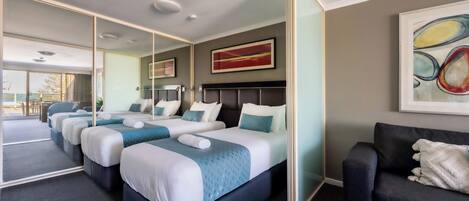 A hotel room with three beds, a sofa, a large mirror, and artwork on the walls.