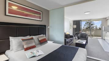 Een hotelkamer met een groot bed, een bureau, een stoel en een balkon met uitzicht op bomen.