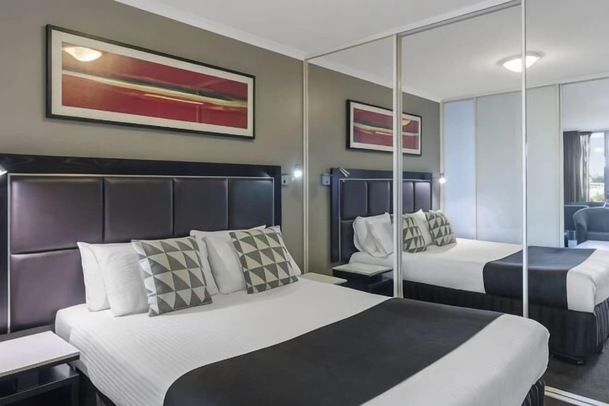 Een hotelkamer met twee bedden, een grote spiegel en kunstwerken aan de muur.