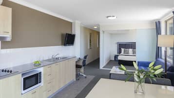 Cozinha moderna com micro-ondas, pia e armários, área de jantar com mesa e cadeiras, e sala de estar com sofá e televisão.