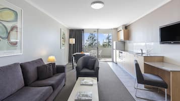 Een moderne hotelkamer met een bank, fauteuil, salontafel en een kleine kitchenette met een televisie.