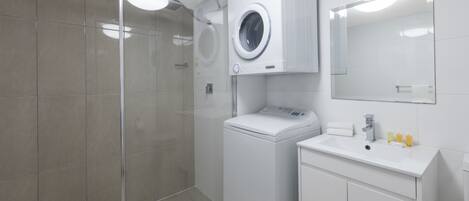 Un baño moderno con cabina de ducha de vidrio, lavadora integrada y lavamanos con espejo superior.