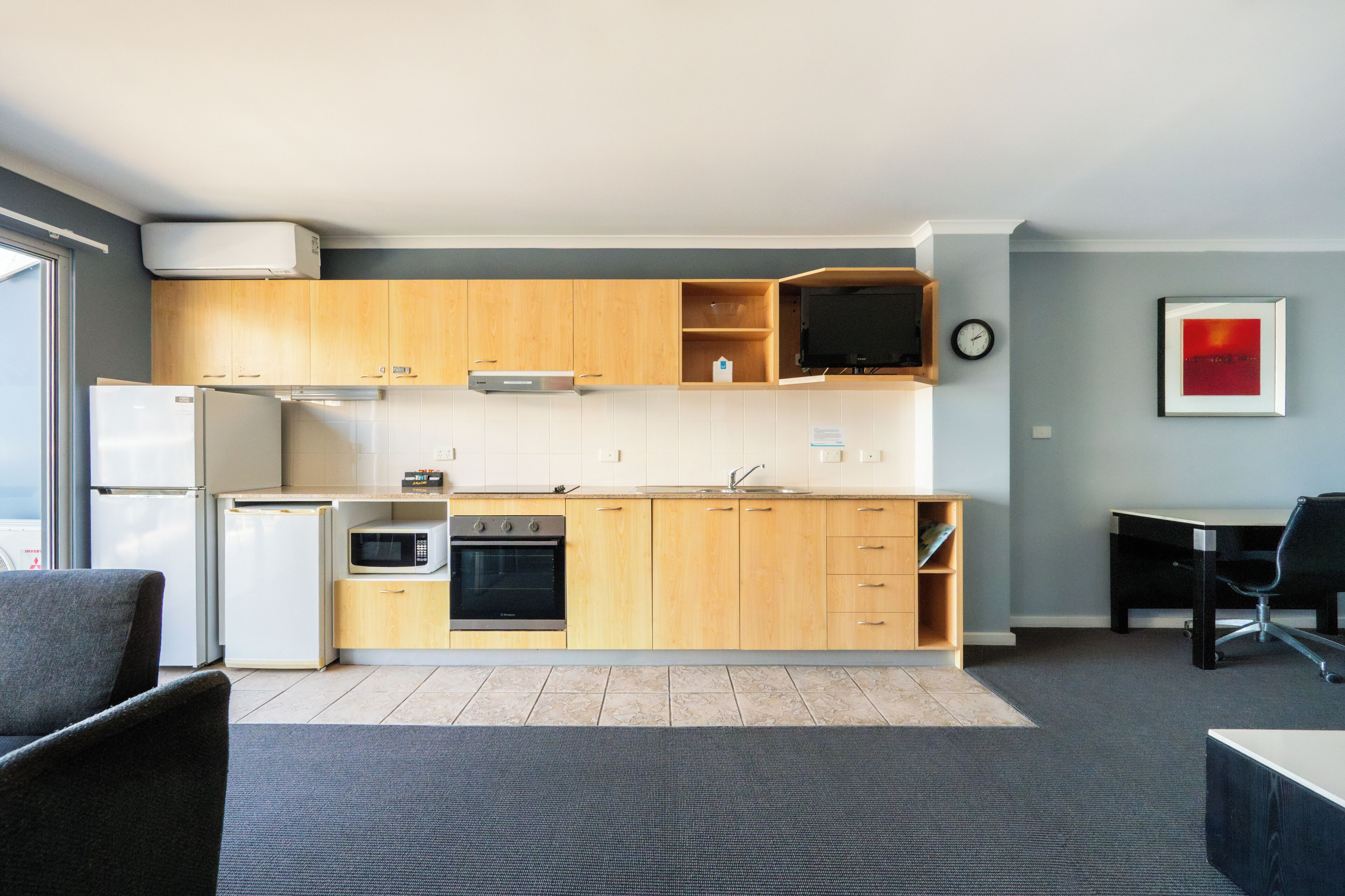 A modern kitchen with wooden cabinets, a microwave, a refrigerator, and a stove. There is a dining table and chairs in the adjacent dining area.