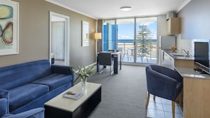 A modern hotel room with a balcony, a sofa, a dining area, and a kitchenette.