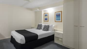 A hotel room with a bed, a wardrobe, a nightstand, and two framed pictures on the wall.