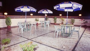 Un patio al aire libre con mesas, sillas, sombrillas y plantas en macetas.