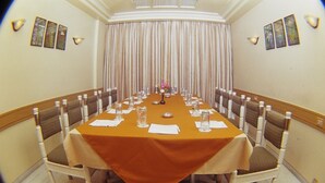 Un salón de conferencias con una larga mesa, sillas y un fondo de cortina.