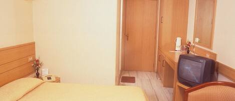 A hotel room with a bed, a desk with a television, a chair, a mirror, and a door.