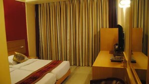 Una habitación de hotel con cama, un escritorio con lámpara y un amplio ventanal con cortinas.