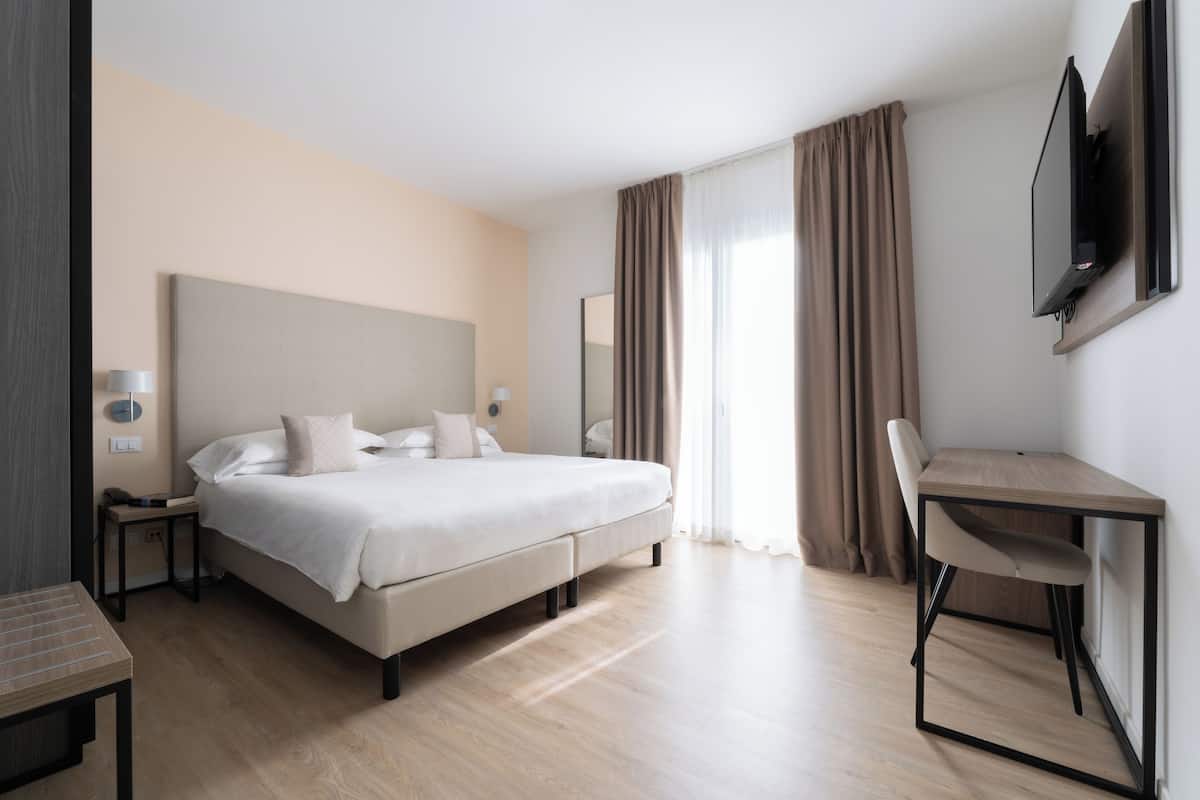 A modern hotel room with a large bed, a desk, and a flat-screen TV mounted on the wall.