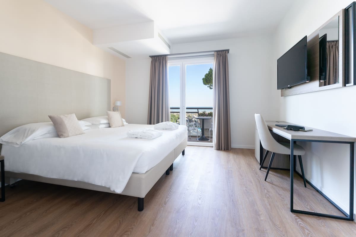 A modern hotel room with a bed, a desk, and a balcony with a view.