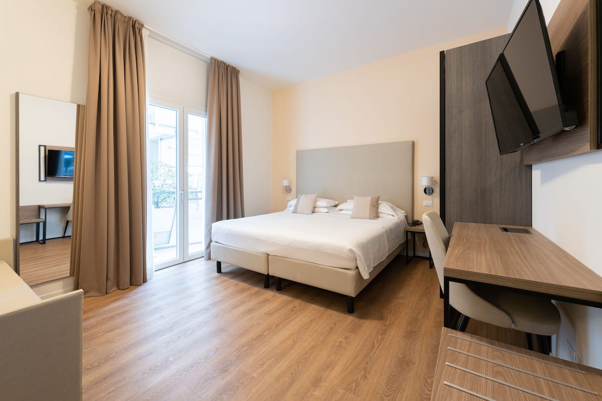A modern hotel room with a large bed, a desk, and a TV mounted on the wall.