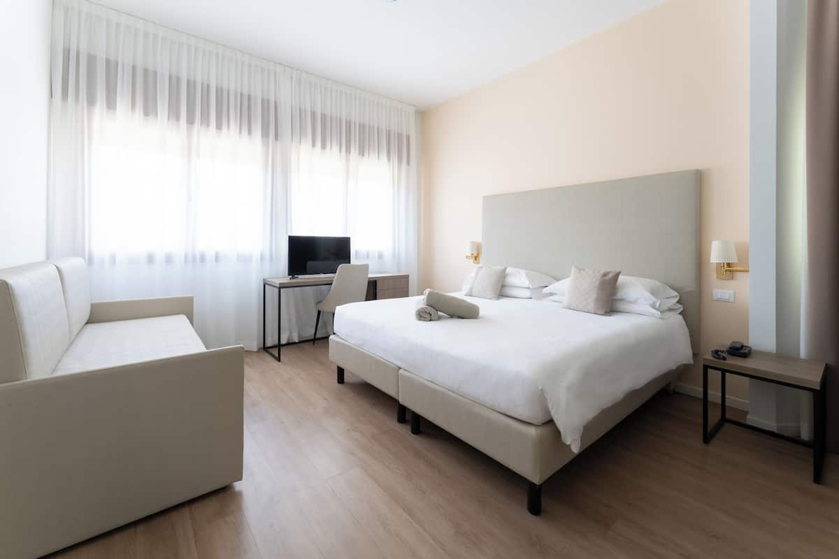 A modern hotel room with a large bed, a desk, a chair, and a television.
