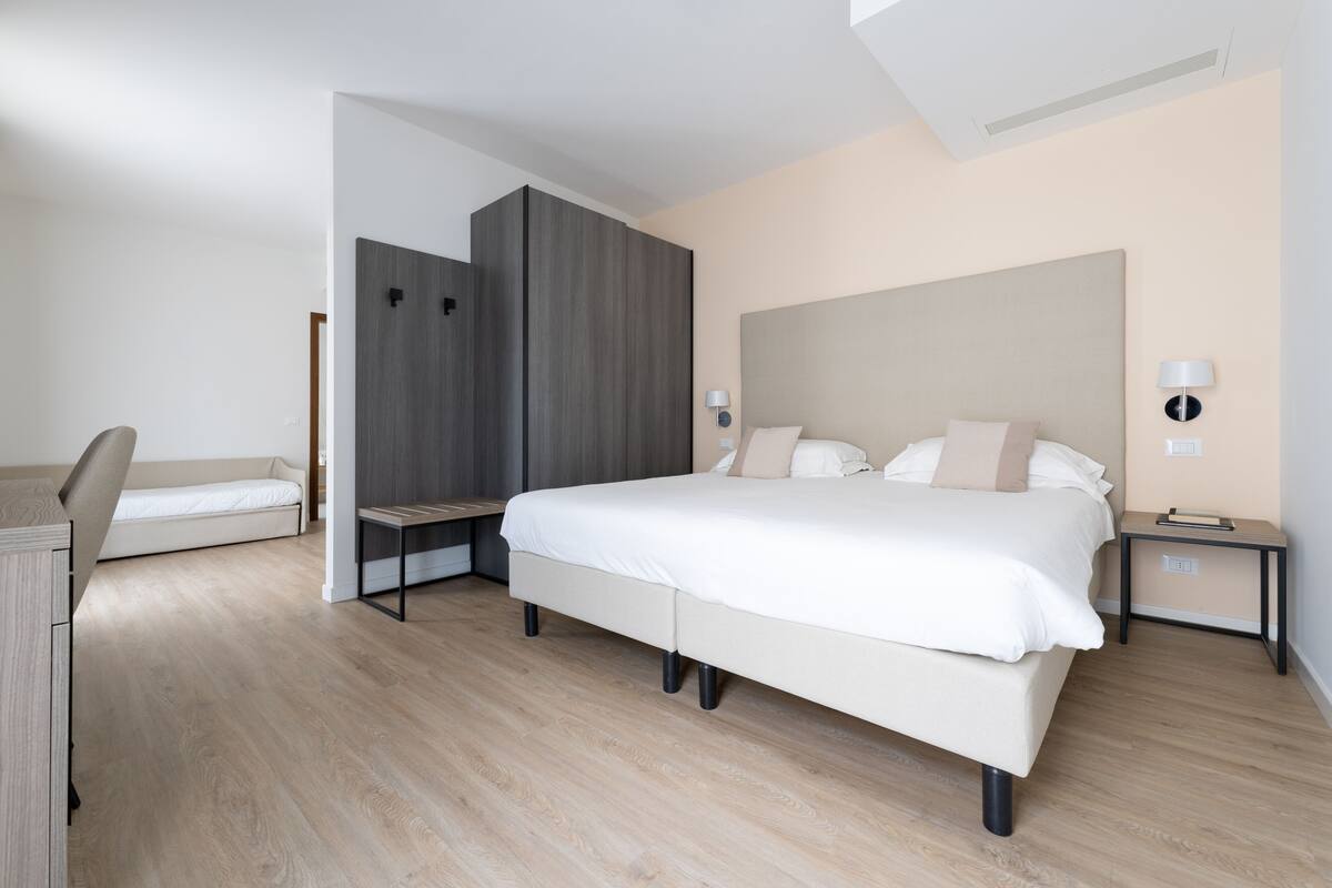 A modern bedroom with a large bed, bedside tables, a desk, and a wardrobe.