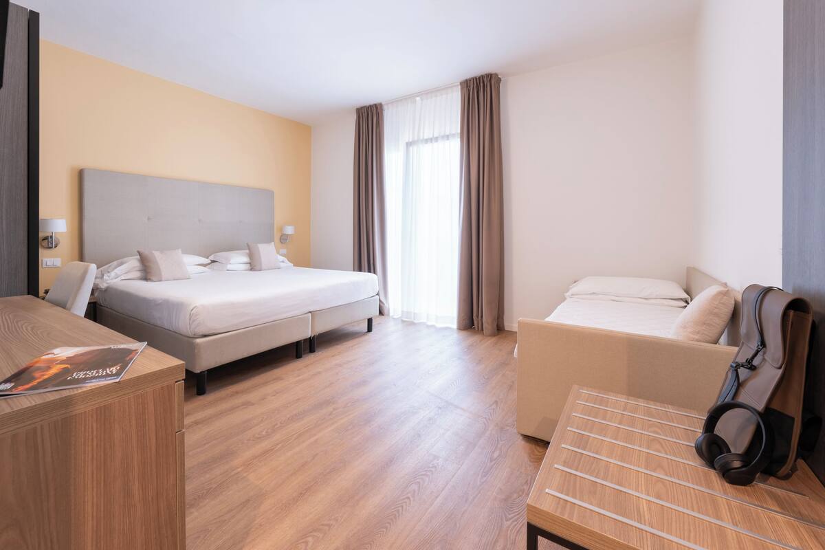 A hotel room with a bed, a desk, a chair, and a coat rack.