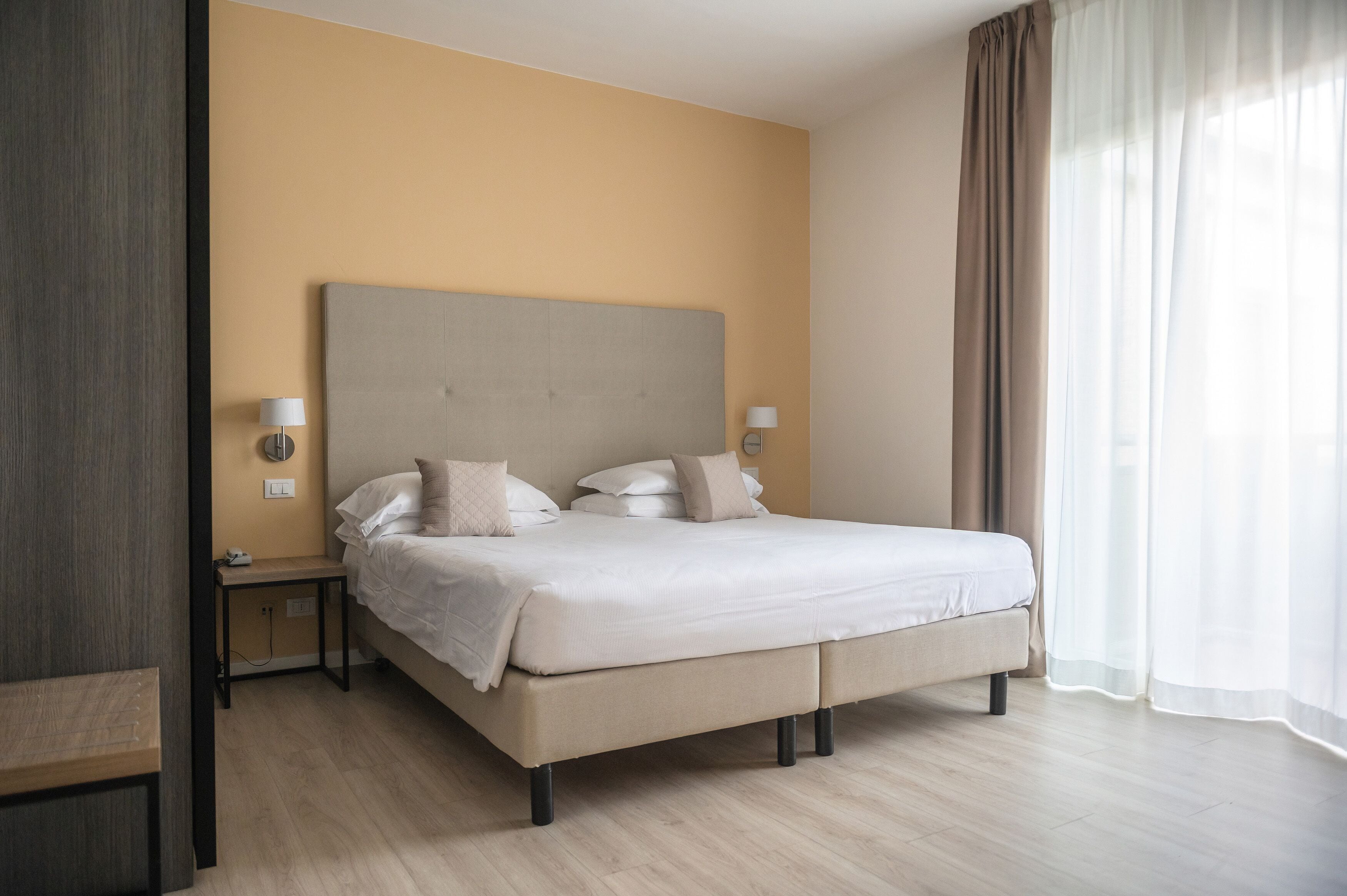 A modern hotel room with a large bed, bedside tables, and a view of the outdoors.