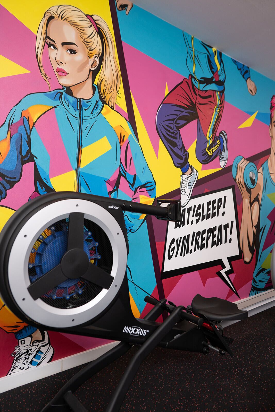 A stationary bike with a colorful mural in the background, including a motivational phrase.