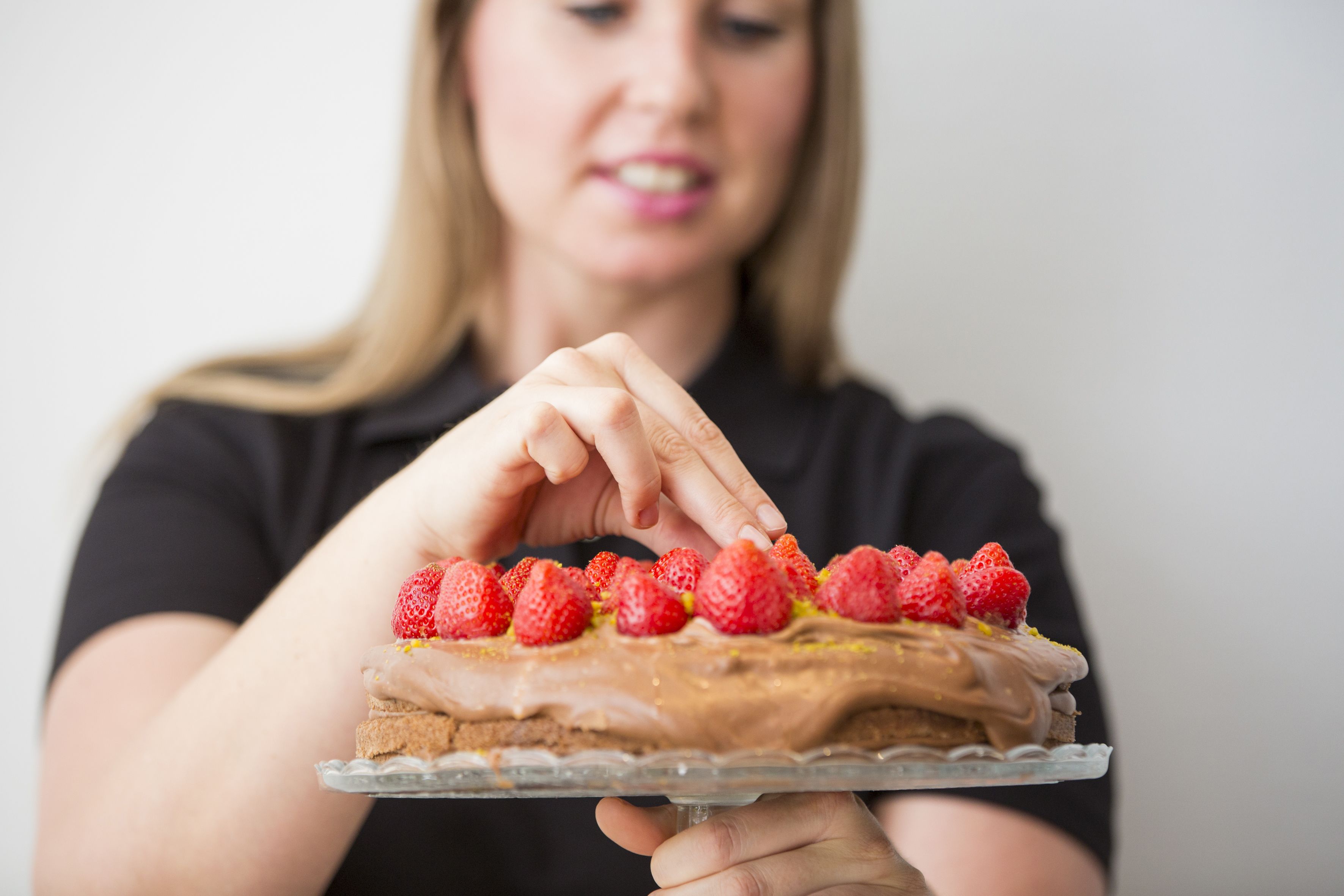 En person håller i en chokladtårta med jordgubbar på en genomskinlig glastallrik.
