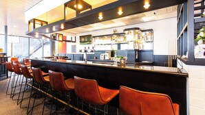 Eine Bar mit einer langen Theke, mehreren Barhocker und einer modernen Küche im Hintergrund.