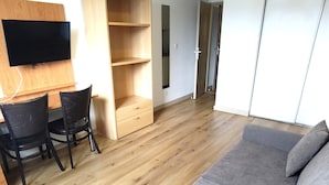 Een moderne woonkamer met een grijze bank, houten vloeren, een aan de muur bevestigde televisie en een houten dressoir.