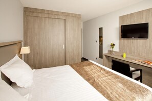 Une chambre d’hôtel comprenant un lit, un bureau, une chaise, une télévision et une armoire.