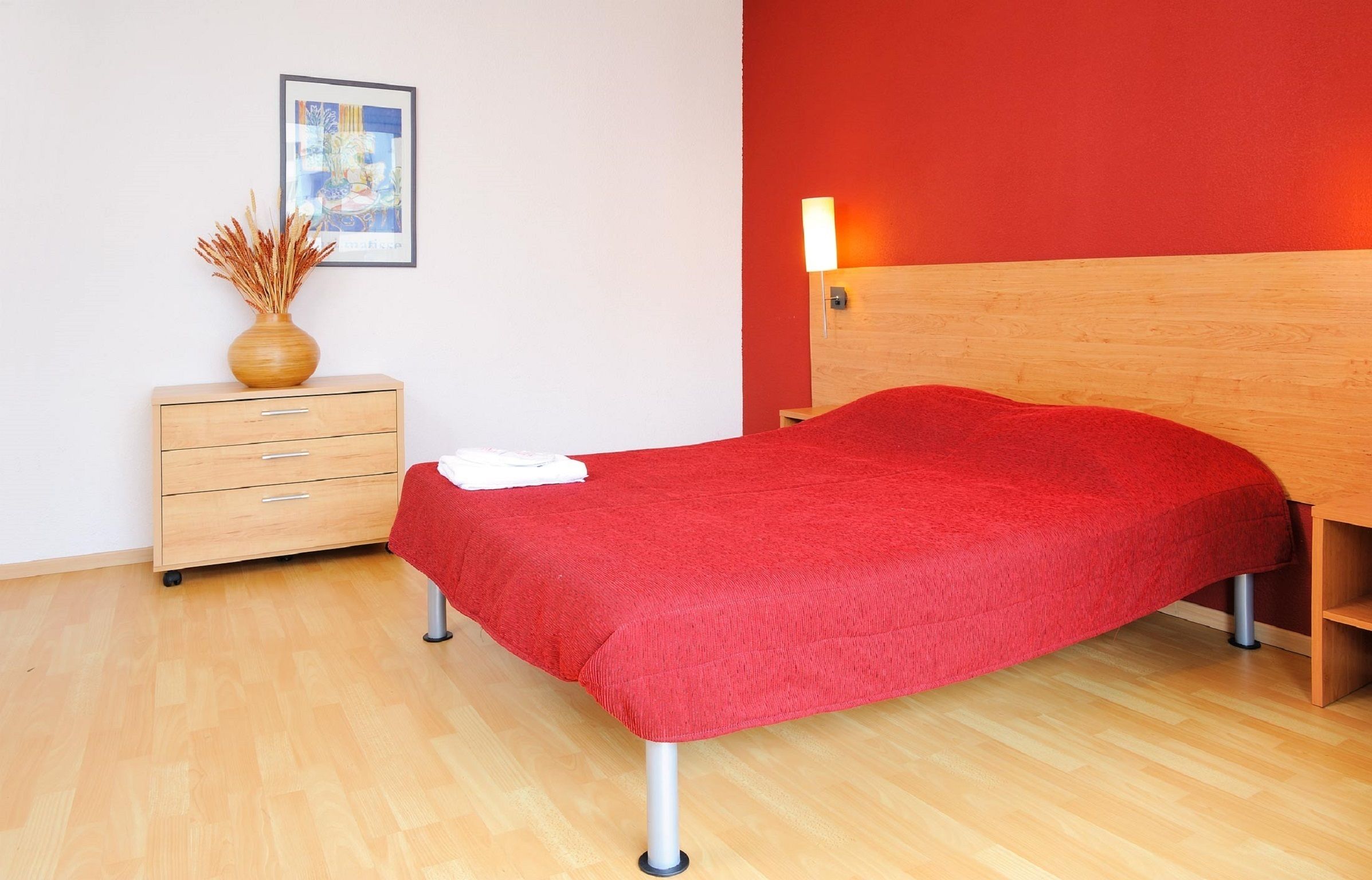Une chambre à coucher avec un lit en bois, une table de chevet sur laquelle se trouve un vase, et un tableau encadré accroché au mur.