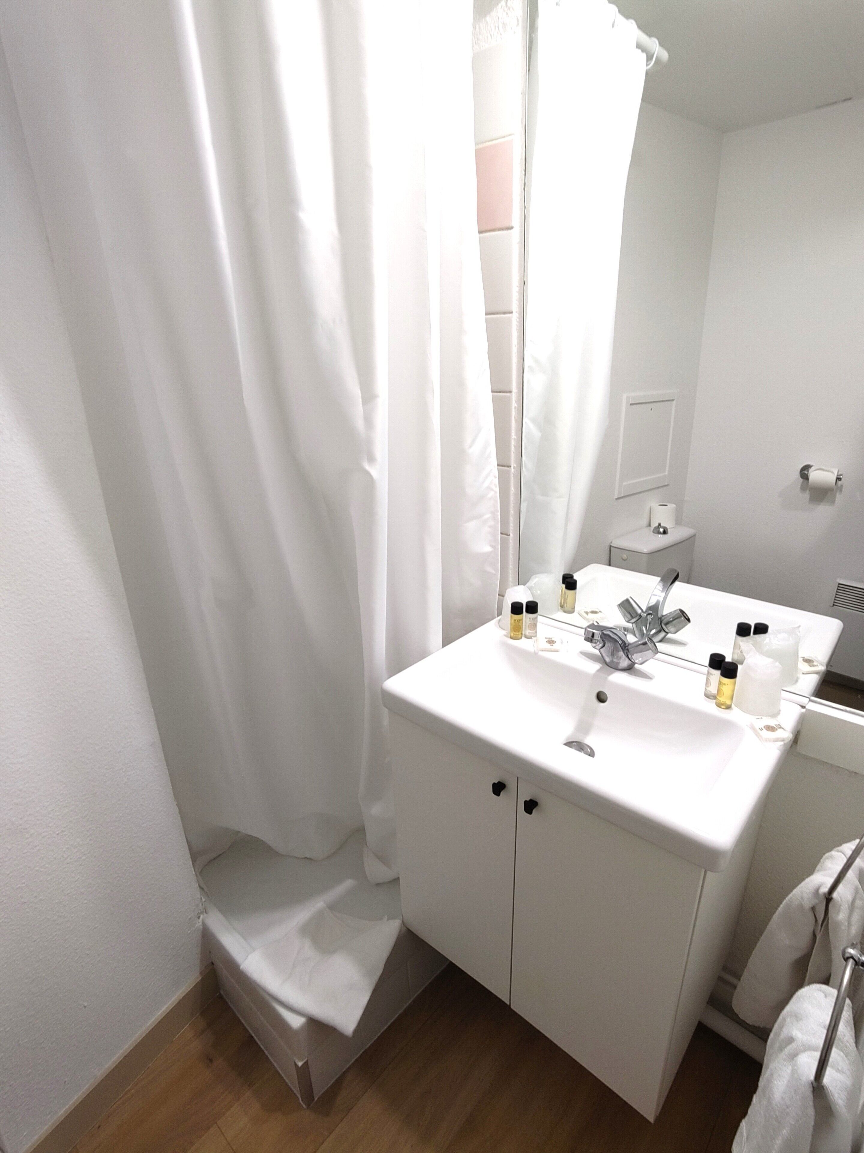 Une salle de bain avec un lavabo blanc, un miroir et un rideau de douche.