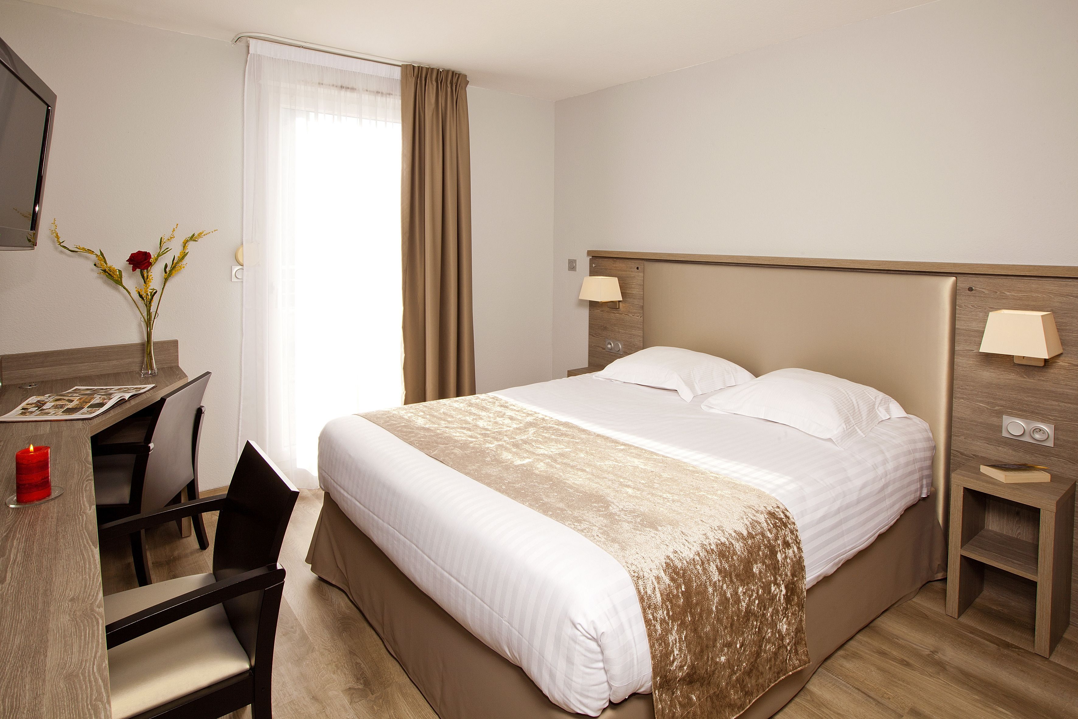 A hotel room with a bed, bedside tables, a desk, and a chair.