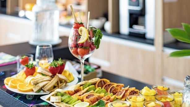 Een buffet met diverse soorten fruit, groenten en een glas met aardbeien en citroenpartjes.