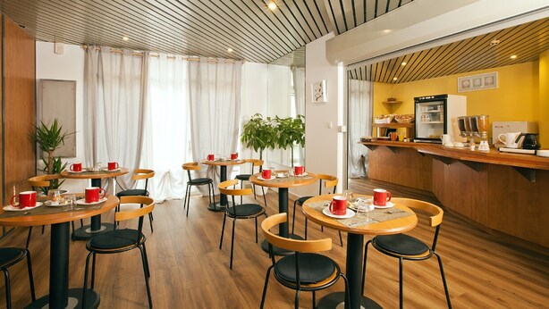 A modern cafe with round tables, black chairs, and a wooden ceiling. - Séjours & Affaires Strasbourg Kléber (Strasbourg)