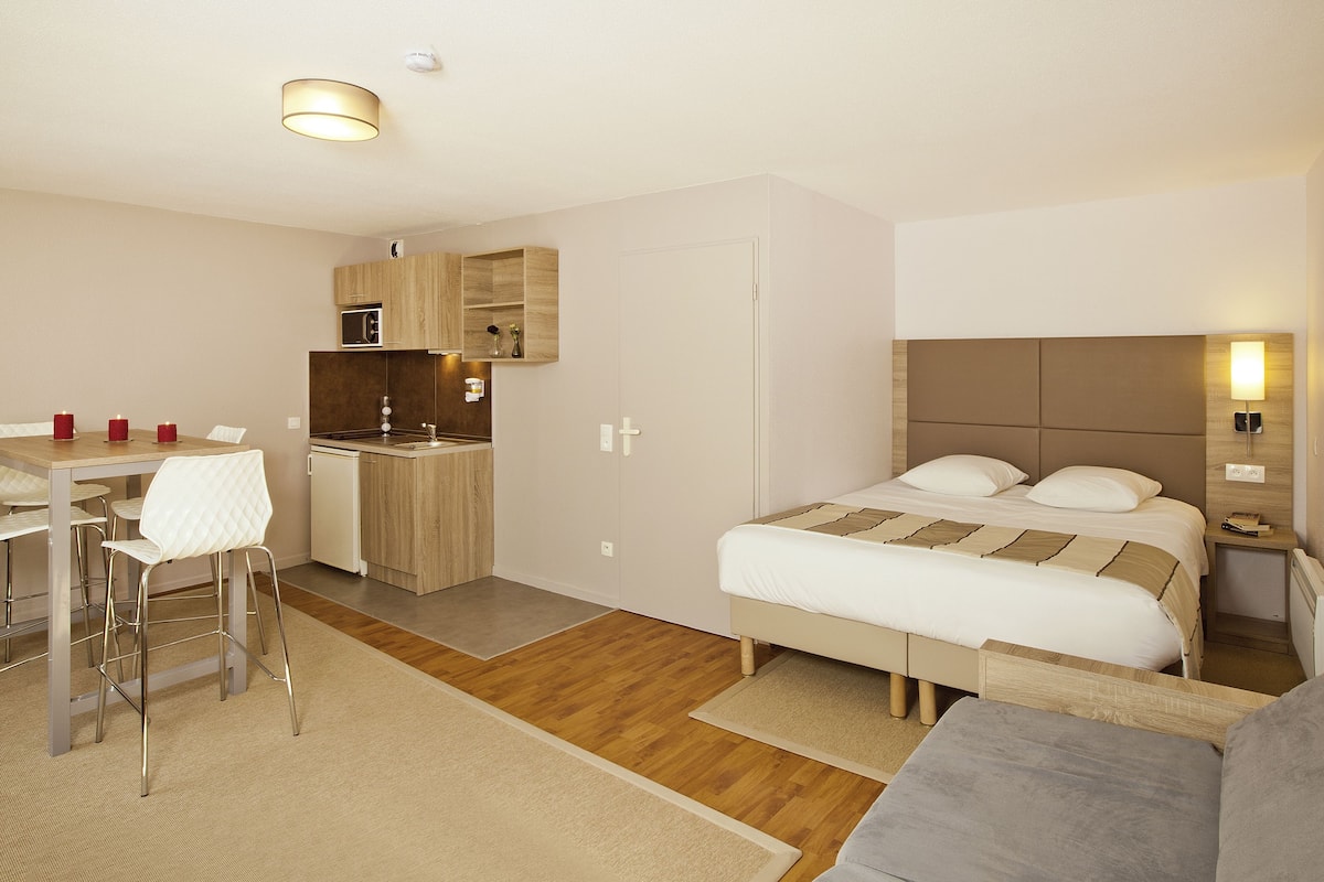 Moderni hotellihuone, jossa on sänky, pieni keittonurkkaus, ruokailutila ja erillinen oleskelualue.