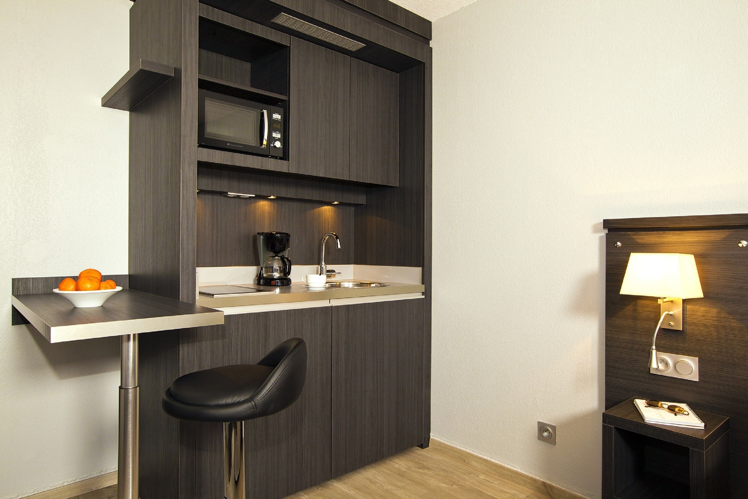 Una cocina compacta con microondas, cafetera y un taburete pequeño.