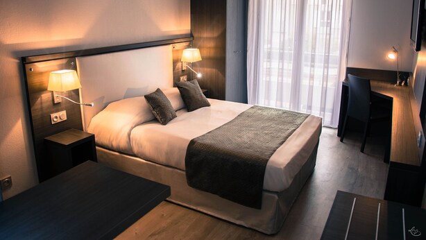 A modern hotel room with a large bed, bedside lamps, a desk, and a chair.