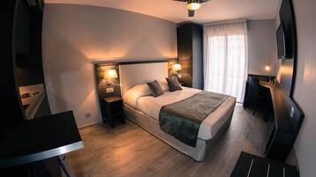 Une chambre d’hôtel moderne équipée d’un lit, de lampes de chevet, d’un ventilateur de plafond, d’une télévision et d’un bureau.
