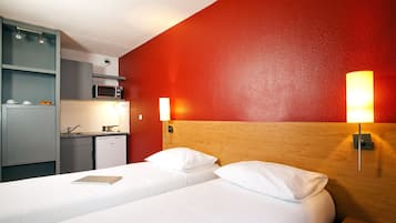 Une chambre d’hôtel comprenant un lit, des lampes de chevet, une table de chevet avec des verres, un petit coin cuisine équipé d’un four à micro-ondes et un mur d’accent de couleur rouge.