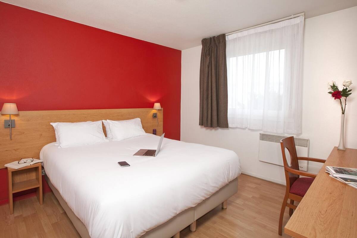 Une chambre d’hôtel avec un grand lit, une table de chevet en bois, un bureau avec une chaise et une fenêtre avec des rideaux.
