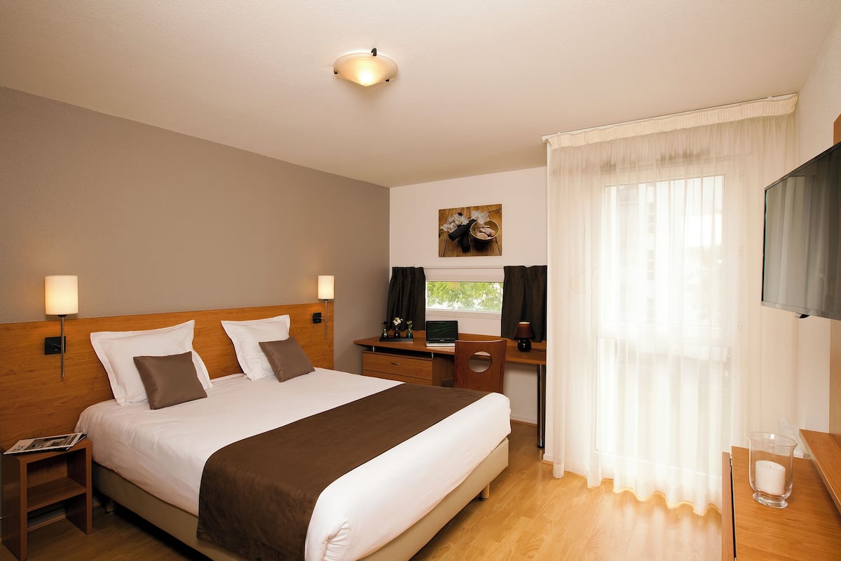 Une chambre d’hôtel avec un grand lit, un bureau, une chaise, une télévision et une fenêtre avec des rideaux.