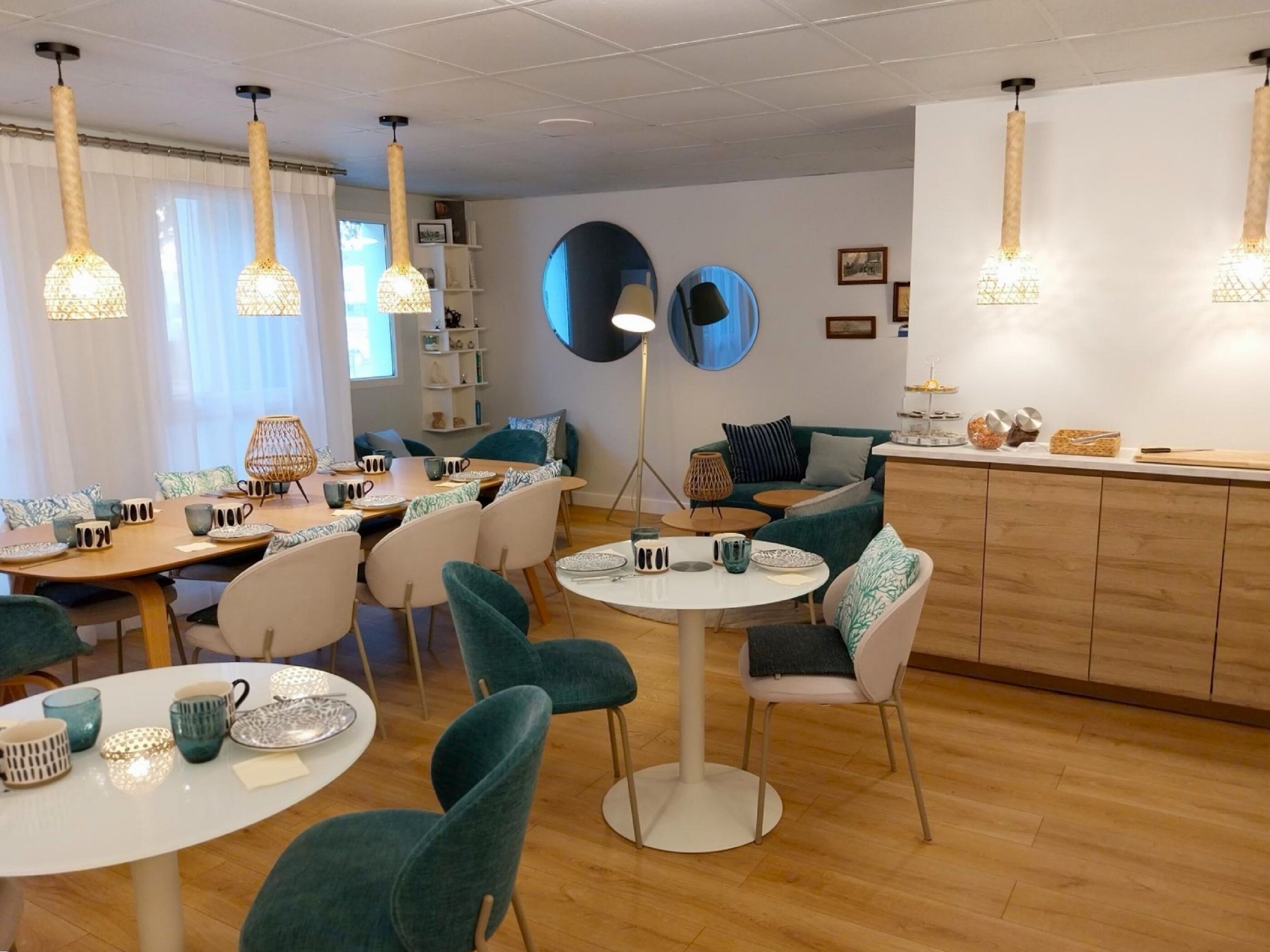 Een moderne eetruimte met ronde tafels, teal stoelen en hangende hanglampen.