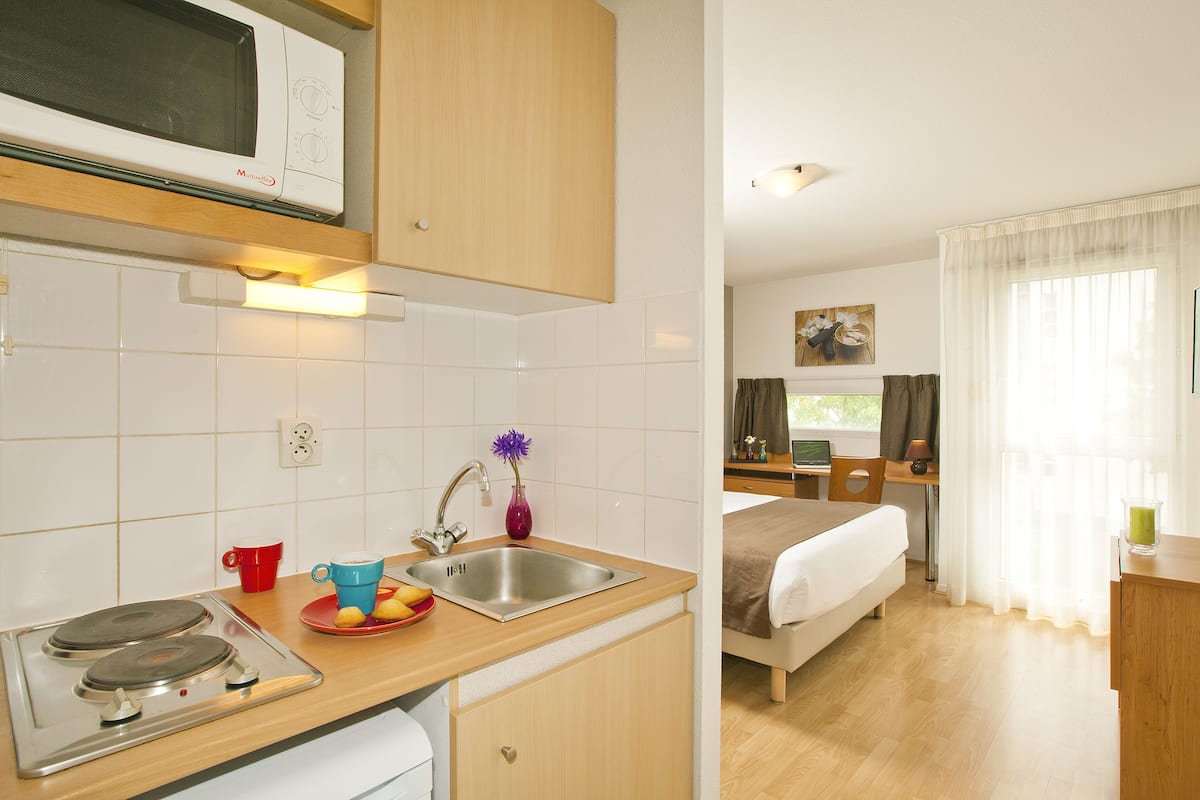 Une cuisine compacte équipée d’un four à micro-ondes, d’un évier et d’une cuisinière, ainsi qu’une chambre avec un lit et une fenêtre.
