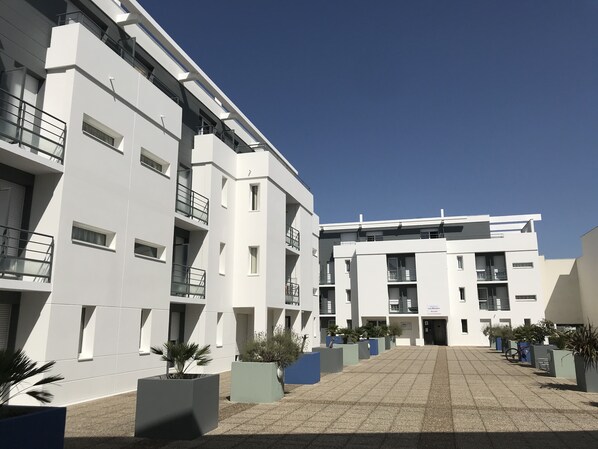 A modern building with multiple floors, balconies, and a paved courtyard.