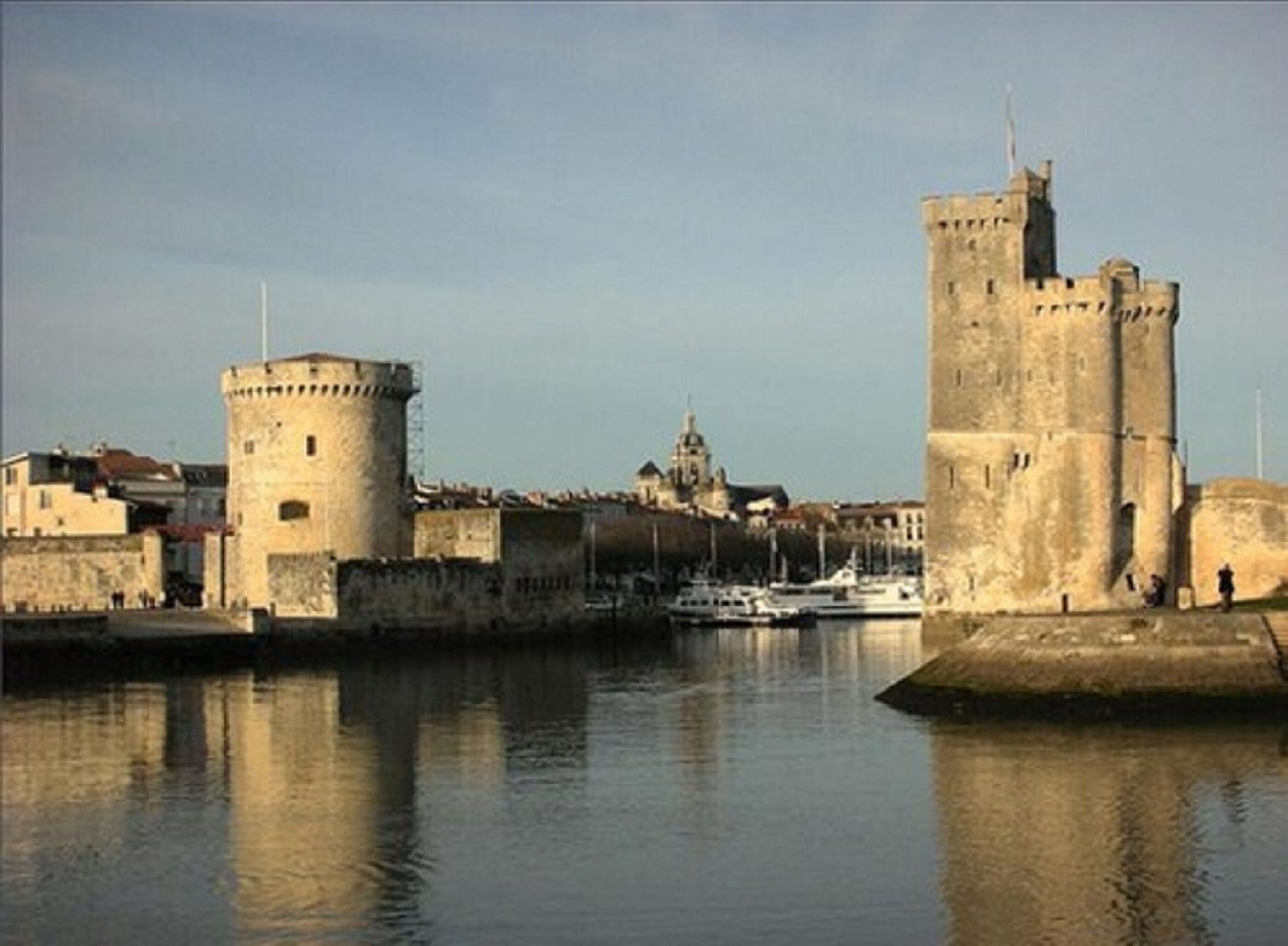 Un castillo de piedra histórico con una torre destacada, ubicado junto a un cuerpo de agua tranquilo con barcos amarrados cerca.