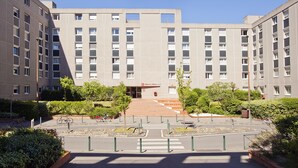A multi-story building with a central entrance, surrounded by greenery and a pedestrian pathway.